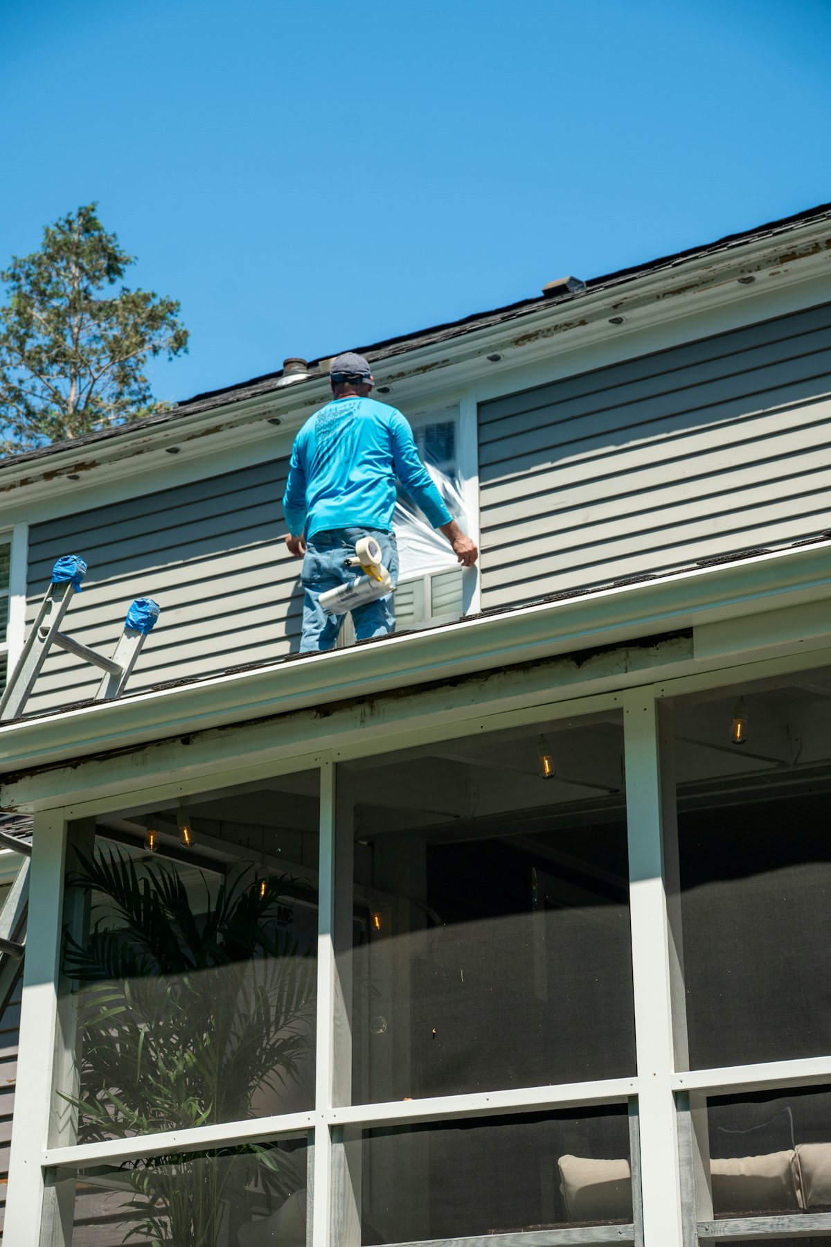 A tradesman working on siding and a window from the roofline of a two-story home