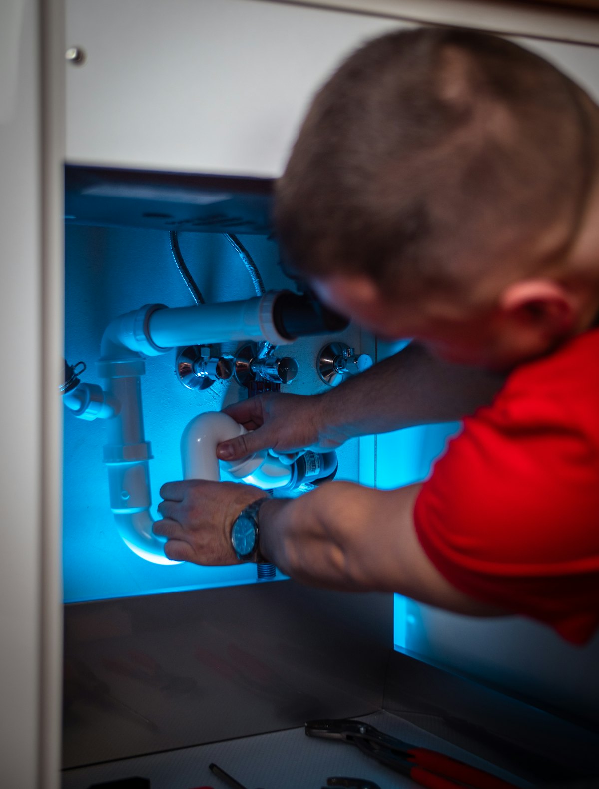 A plumber reconnecting the drain under a kitchen sink.