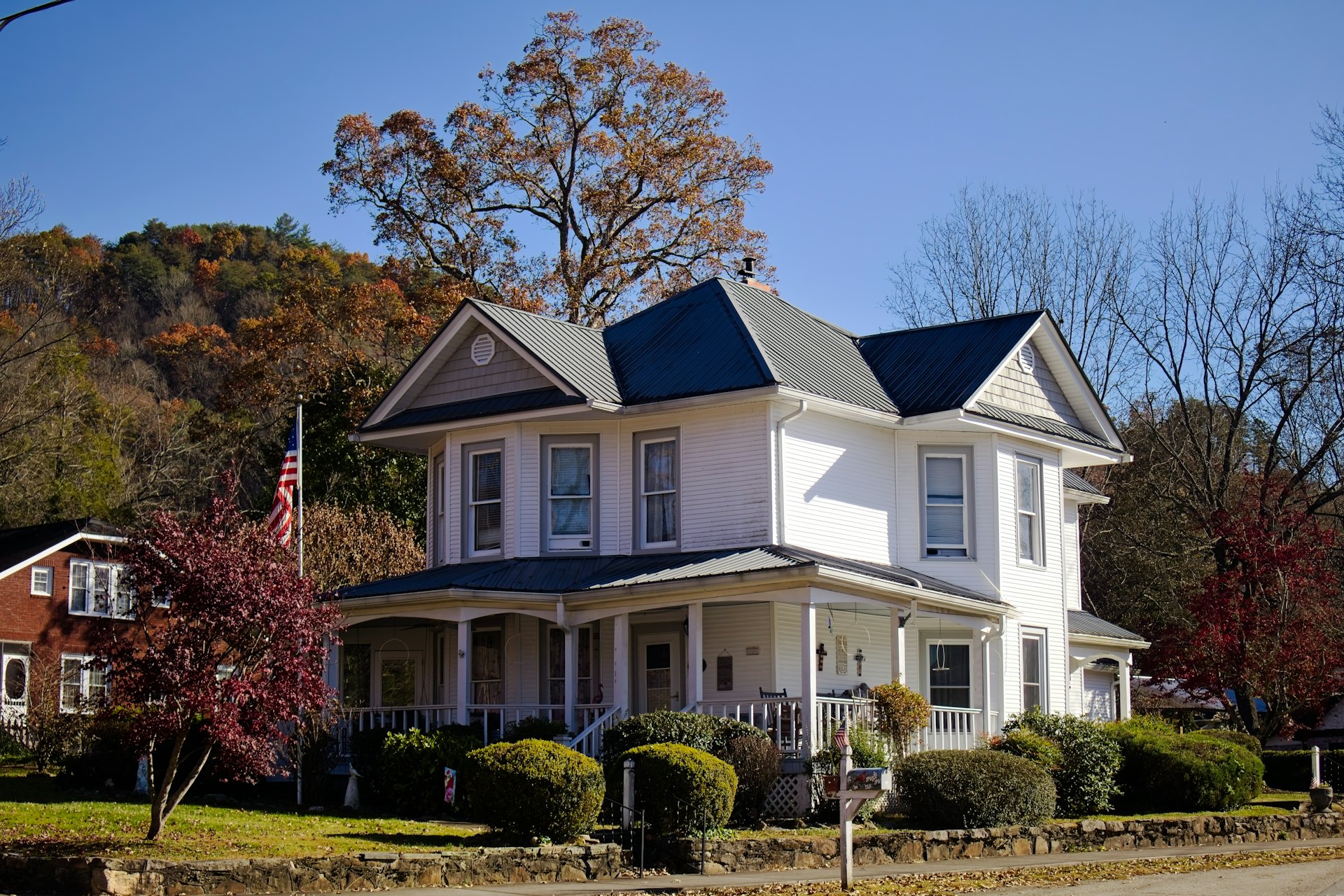 A white two-story home with a wraparound porch in autumn