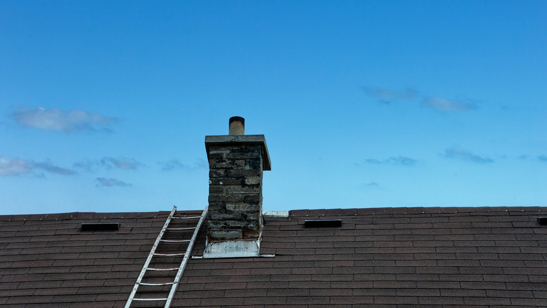 A stone chimney and ladder on a shingle roof